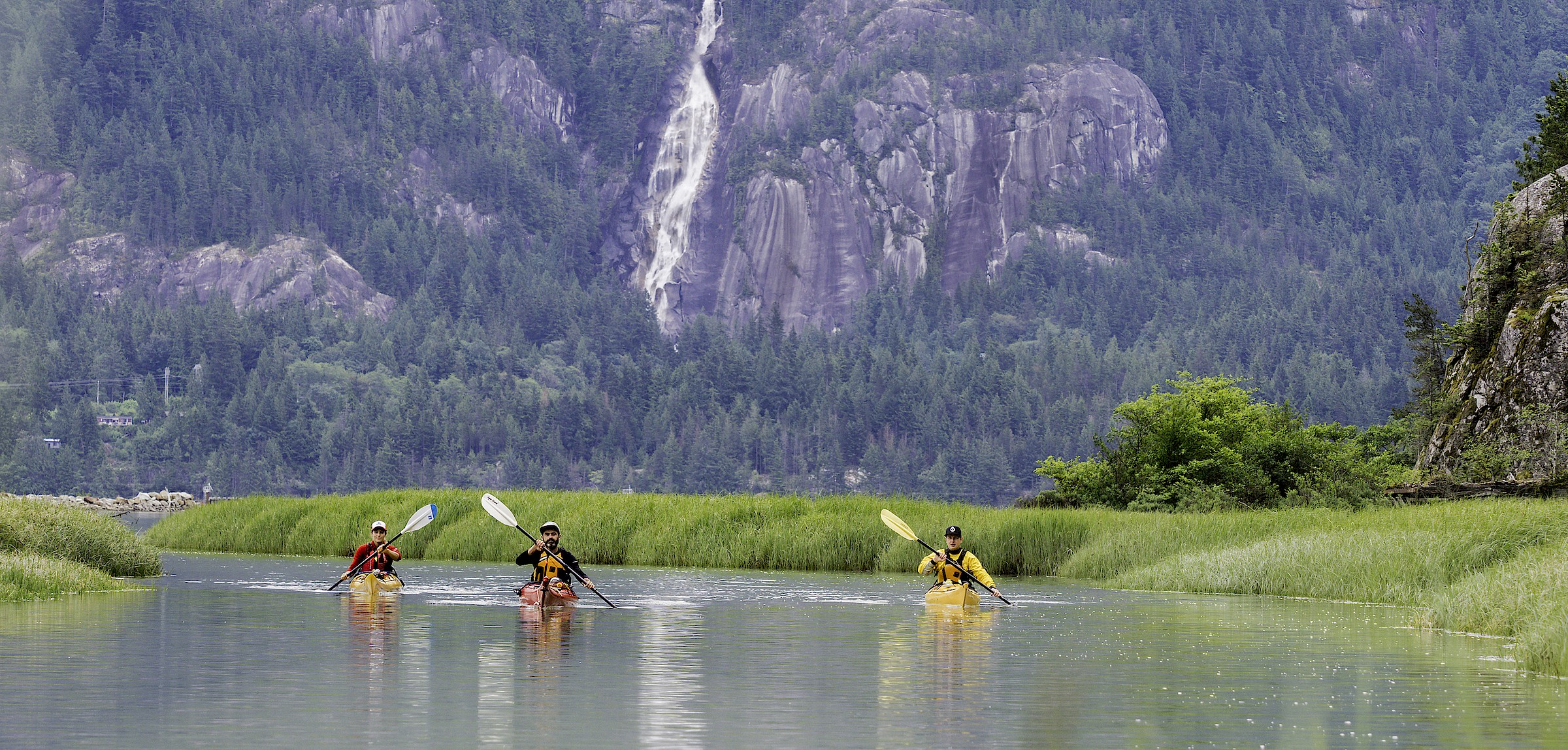 Group of 3 kayakers paddling in the Squamish Estuary with Shannon Falls behind